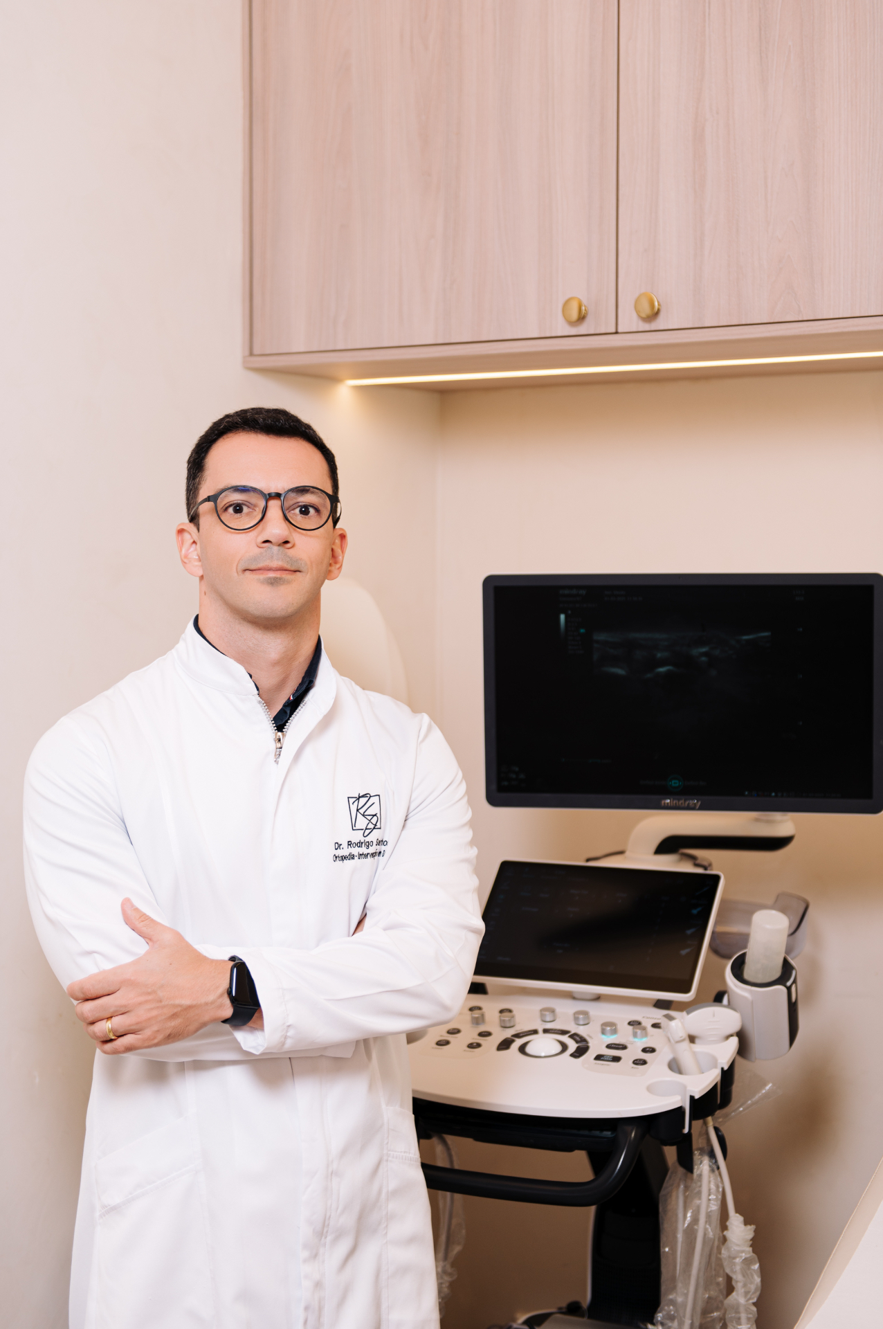 Dr. Rodrigo Santos no consultório ao lado de equipamento de ultrassom